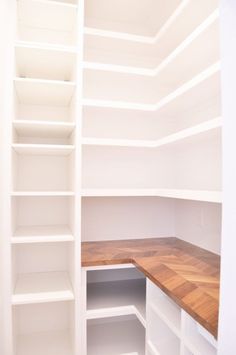 an empty closet with white shelves and wood counter tops