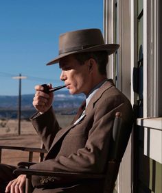 a man in a suit and hat sitting on a chair with a pipe in his mouth