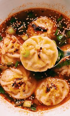 a white bowl filled with soup and dumplings on top of sesame seed sprinkles