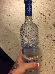 a woman's hand holding up a bottle of grey goose vodka with a crown on it