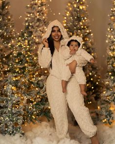 a woman holding a baby while standing in front of a christmas tree with lights on it