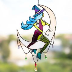 a stained glass sun catcher with a woman sitting on the moon hanging from it's side