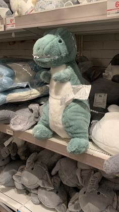 a stuffed dinosaur sitting on top of a shelf in a store filled with blankets and t - shirts