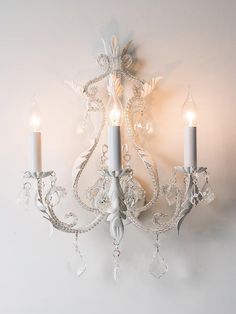 a white chandelier with two candles hanging from it's sides and one light on the wall