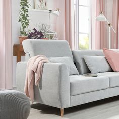 a living room with pink curtains and grey couch in front of the window, next to a potted plant