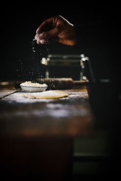 a person sprinkling flour on top of a wooden table