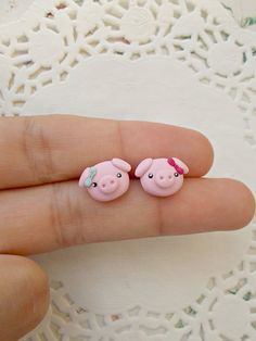 small pink pig earrings sitting on top of a persons finger