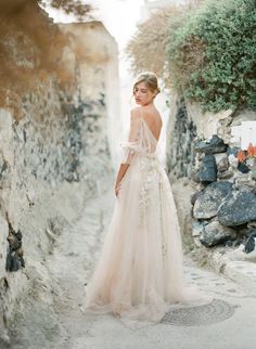 a woman in a wedding dress standing on the side of a stone road with her back to the camera