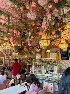 people sitting at tables in a restaurant with chandeliers and flowers hanging from the ceiling