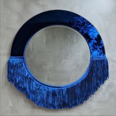 a round mirror with blue fringes hanging on the wall next to a white wall