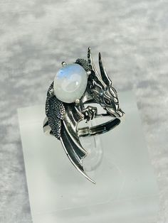 This ring is absolutely beautiful. High Detailed Dragon Ring With Prong Set Smooth Rainbow Moonstone Gemstone - Supplied With Gift Box. Ring is lovingly made of 925 Silver & Stamped 925 The beautiful Moonstone Cabochon Measures 13.6mm x 10.5mm and has a Beautiful Blue Flashes. The ring can adjusted from the back, but please be gentle when you adjust, so as not to damage the shape of the ring. The Dragon Design itself Measures 40mm tall x 24.8mm wide. Black Spinel Crystals have been used for the Mystical Gemstone Rings For Formal Occasions, Hallmarked Moonstone Jewelry For Wedding, Hallmarked Moonstone Wedding Jewelry, Silver Mystical Moonstone Ring, Mystical Adjustable Oval Jewelry, Mystical Moonstone Open Ring Jewelry, Mystical Gemstone Rings For Collectors, Mystical Collectible Gemstone Rings, Adjustable Mystical Sterling Silver Rings