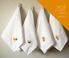 three white towels hanging on a clothes line with embroidered fruit and flower appliques