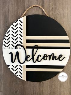 a black and white welcome sign hanging on a wooden wall with the word welcome painted on it