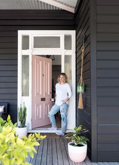 a woman standing in the doorway of a house with potted plants on the porch