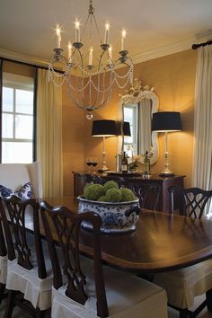 a dining room table with chairs and a bowl of fruit on it in front of a chandelier