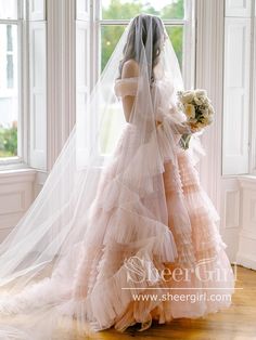 a woman standing in front of a window wearing a wedding dress and holding a bouquet