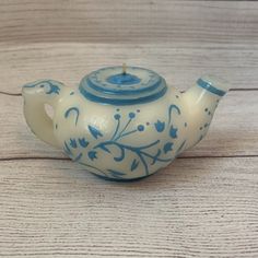 a blue and white teapot sitting on top of a wooden table next to a candle