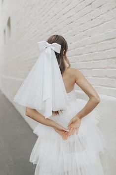 a woman in a white dress with a veil on her head and hands behind her back