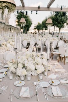 a table set up with white flowers and silverware for a formal dinner or reception