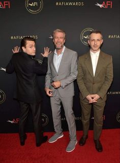 three men in suits standing on a red carpet with their hands up to the camera