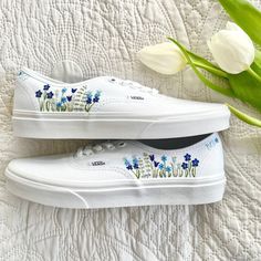 two white vans with blue flowers painted on them sitting next to a tulip plant