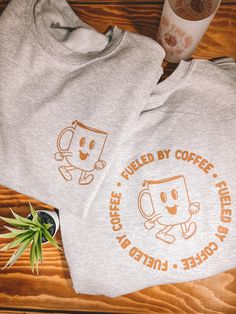 "Fueled by coffee" repeat screen print crewneck sweatshirt designed/illustrated by me. The shirt features a front and back design! This cozy sweatshirt is for all my fellow coffee lovers out there! Wear it to the coffee shop, at home while reading a good book and drinking coffee, to the book store, or anywhere your heart desires, as it will quickly become your new favorite! this item is made to order.  FRONT DESIGN:  Coffee character printed on the left chest. BACK DESIGN:  Coffee character in the middle of a repeat "Fueled by coffee" circle of text.  MATERIAL & FIT: This is a true to size unisex t-shirt in the color ash. 9 oz 50/50 cotton poly blend Gildan brand.  Moisture-wicking properties. Spandex in collar, cuffs, and waistband **For an oversized look I would size up 1 size. Your regu Coffee Color Graphic Print Crew Neck Sweatshirt, Coffee Colored Cotton Sweatshirt With Letter Print, Coffee-colored Relaxed Fit Sweatshirt With Letter Print, Coffee-colored Graphic Print Sweatshirt For Fall, Coffee Colored Relaxed Fit Sweatshirt With Letter Print, Relaxed Fit Coffee Sweatshirt With Letter Print, Relaxed Fit Coffee Cotton Sweatshirt, Relaxed Fit Cotton Sweatshirt In Coffee Color, Coffee Shop Merchandise