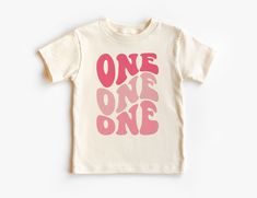 Retro First Birthday Toddler Shirt - Girls Pink Groovy 1ST Birthday Kid's Tee - One Birthday Party Theme - Boho Natural Toddler & Youth Tee If you love super soft, lightweight, extremely comfy shirts and baby bodysuits then you will absolutely love our unisex kids shirts and baby bodysuits! These shirts are hand printed with a professional garment printer for a soft, durable, long lasting, printed graphic using high quality water based inks. * The printed design is very soft to the touch due to Pink Number Print T-shirt For Birthday, Pink Crew Neck Top For First Birthday, Pink Short Sleeve T-shirt With Number Print, Pink Birthday Shirt For Summer, Pink Summer Birthday Shirt, Pink Graphic Print Top For Birthday, Pink Tops With Letter Print For First Birthday, Pink Crew Neck T-shirt For First Birthday, Playful Pink Top For First Birthday