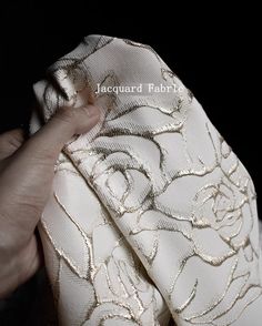 a hand is pulling the fabric off of a white flowered dress with gold sequins