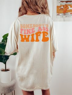 a woman wearing a white shirt that says somebody's fine as wife on it