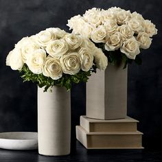 three vases with white roses in them on a table next to books and a plate