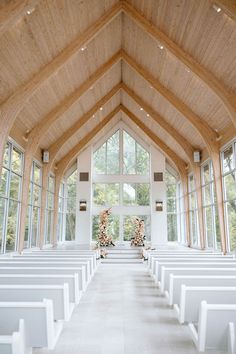 the inside of a church with rows of white benches in front of large windows and wooden ceiling