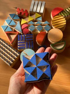 a hand holding a small blue and black origami piece in front of some other colorful shapes