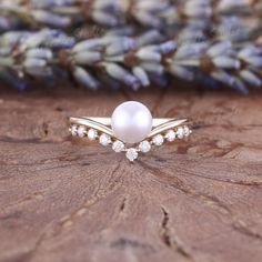 a pearl and diamond ring sitting on top of a piece of wood with lavender flowers in the background