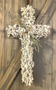 a cross hanging on the side of a wooden wall with white flowers and greenery