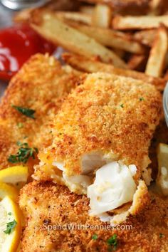 fish and chips on a plate with ketchup, mayonnaise, and lemon wedges