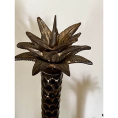 a tall metal vase with leaves in it on a table next to a white wall