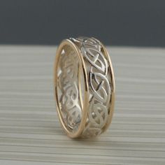 two gold wedding bands with celtic designs on the inside and outside, sitting on top of a wooden table