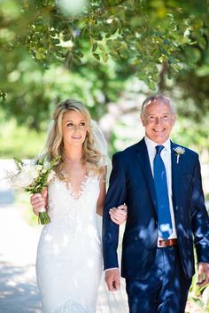 an older man and woman walking down the street with flowers in their hand, holding hands