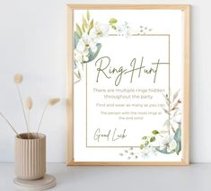 a framed print with the words ring humt and white flowers in gold frame next to a potted plant