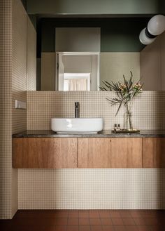 a bathroom sink sitting under a mirror next to a vase with flowers on top of it