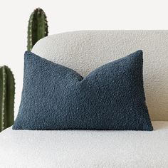 a blue pillow sitting on top of a white couch next to a green cactus plant