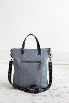 a gray and black handbag sitting on top of a white floor next to a wall