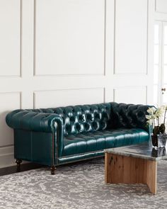 a green leather couch sitting on top of a rug next to a wooden coffee table