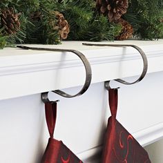 two christmas stockings hanging on a fireplace mantel with pine cones and evergreen branches in the background