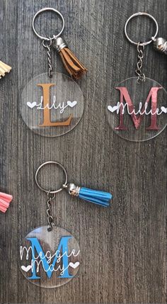 four acrylic keychains with tassels attached to them on a wooden surface