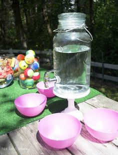 pink bowls and jugs are sitting on a picnic table with an outdoor game area in the background