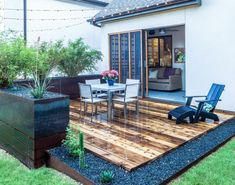 a deck with chairs and table in the middle of a garden area next to a house