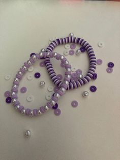 two purple and white bracelets are on a table next to some pearls, beads and other things