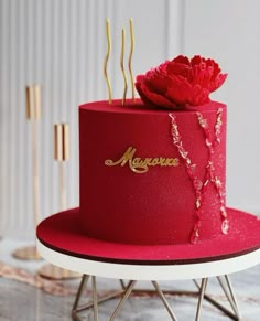 a red cake with gold lettering and a flower on top is sitting on a stand