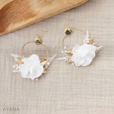 two white flowers are hanging from gold hoop earrings on a table next to a piece of wood